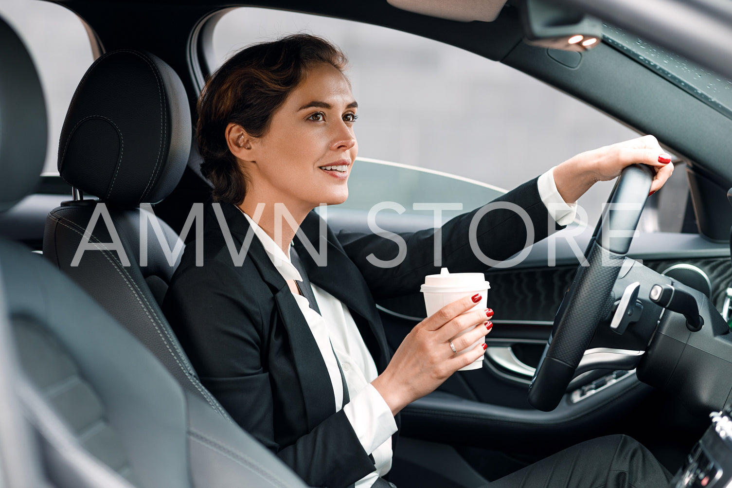 Businesswoman going to office in her car. Side view of female driver holding a coffee.	