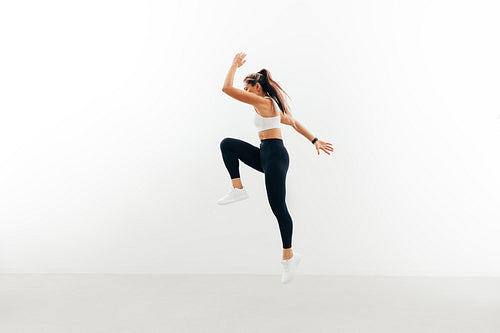 Sportswoman jumping up indoors. Female athlete warming up against a white wall.