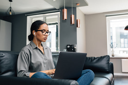 Young woman working from her apartment. Female freelancer using laptop sitting on couch.