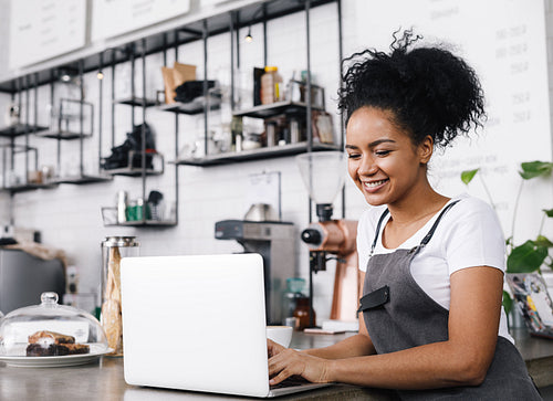 Young cafe owner working on her laptop, standing at counter