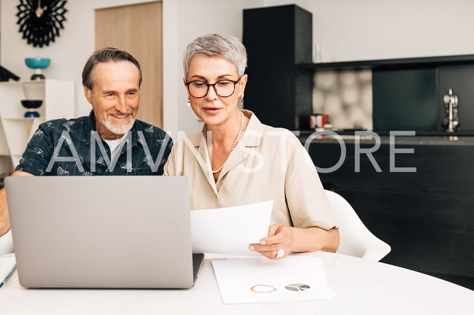 Senior retired couple at a table in dining room using a laptop computer. Two mature people looking at paperwork and discussing their finances.