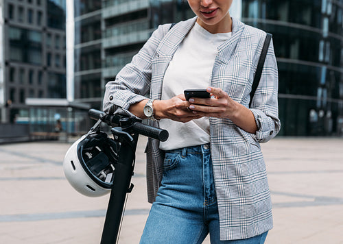 Cropped shot of businesswoman leaning on handlebar of electric scooter using an app for rent