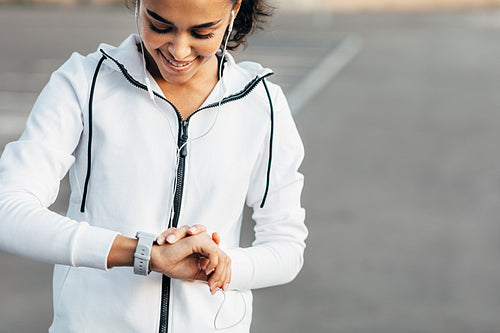 Young woman listening to music with earphones and checking her activity on a smartwatch during training.