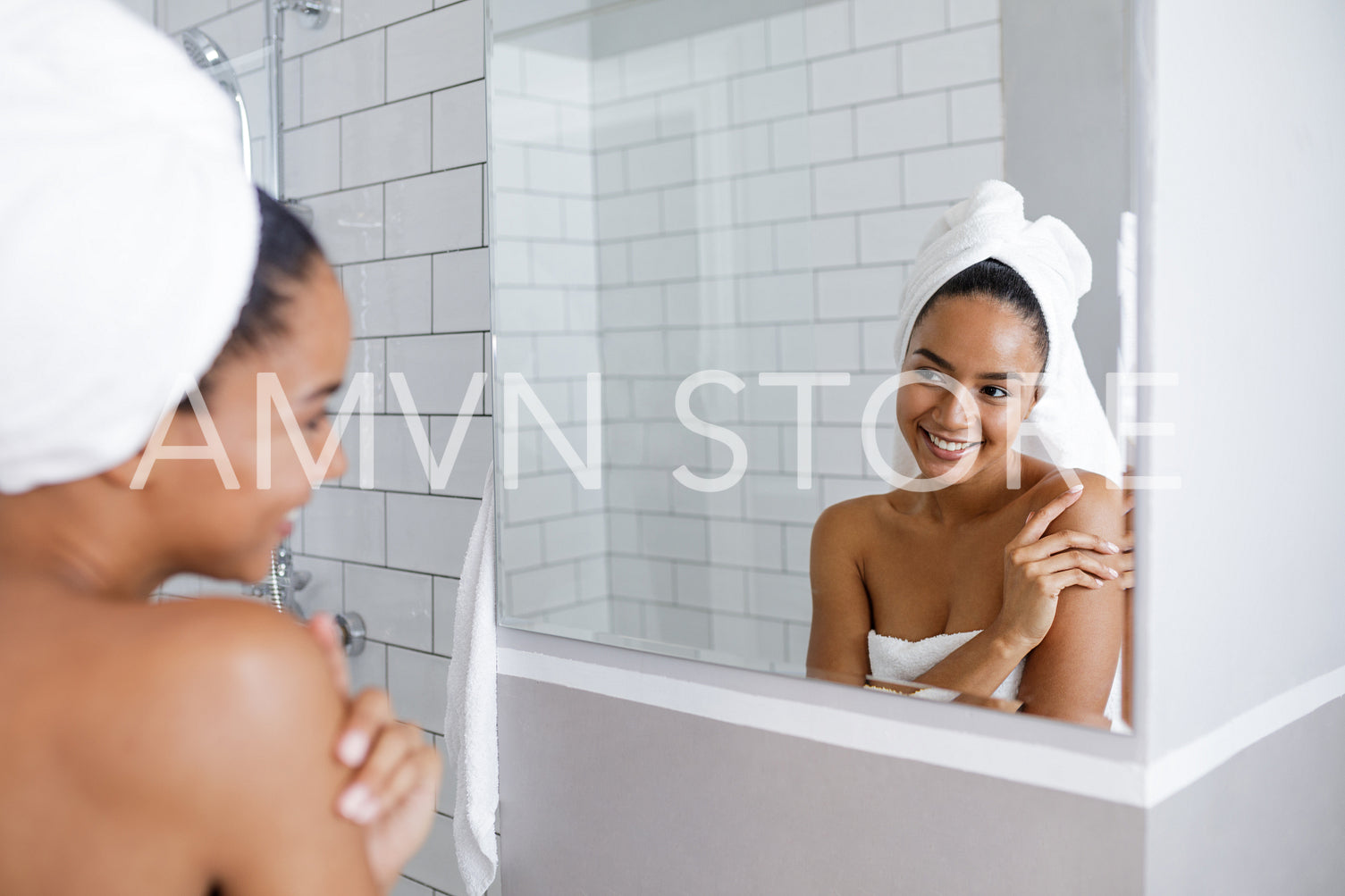 Beautiful mixed race woman looking at her reflection in mirror, touching a shoulder	