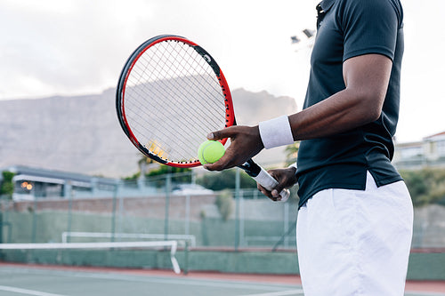 Cropped of an unrecognizable tennis player holding a racket and tennis ball while standing outdoors on a hard court