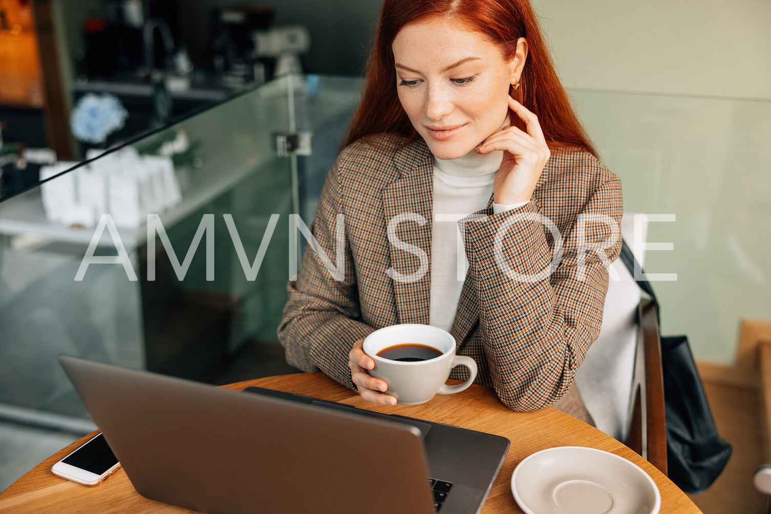 Businesswoman holding a cup of coffee and looking at laptop while sitting in cafe