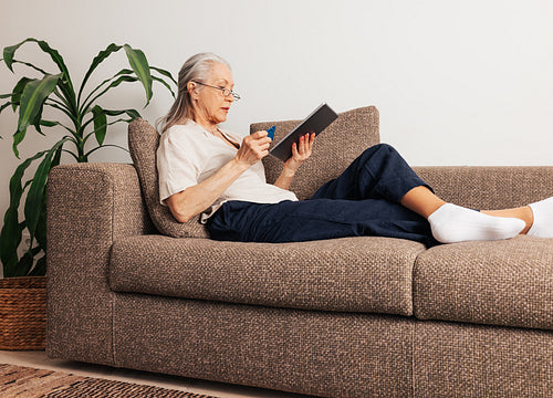 Side view of a senior female holding a credit card and digital tablet. Aged woman renew subscription.