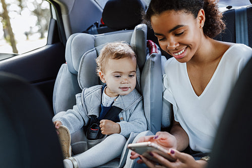 Young mother with her daughter sitting on a backseat of a car. Woman and a little girl looking on cell phone in the car.