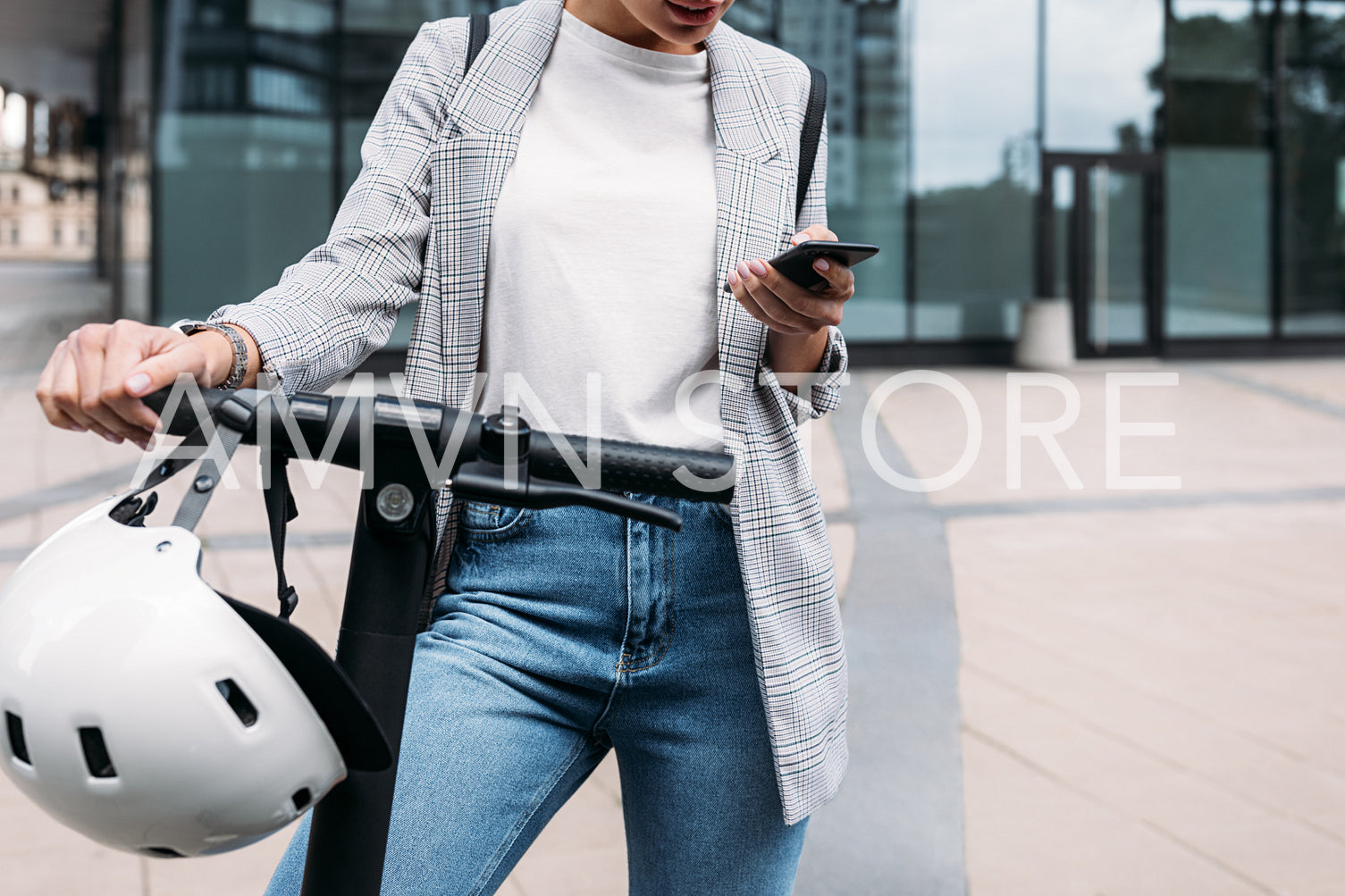 Unrecognizable businesswoman standing at office building with electric scooter holding smartphone