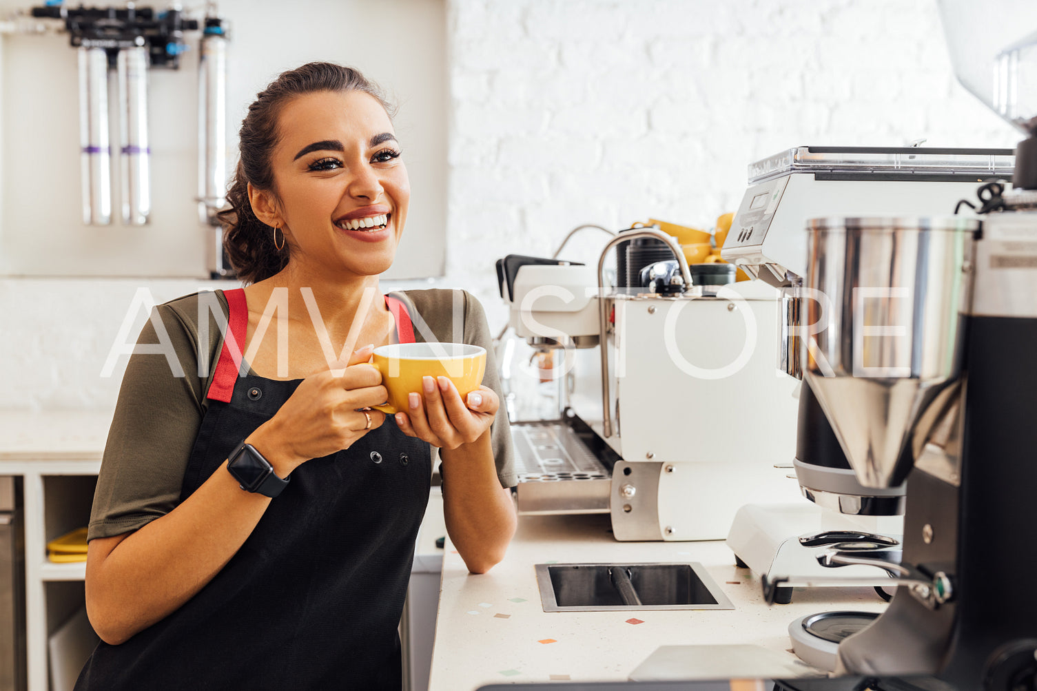 Happy female barista standing at coffee machine and holding a mug. Female cafe worker taking a break.	