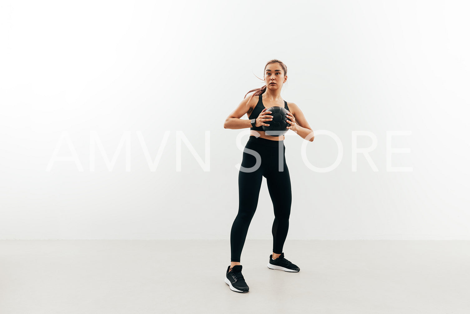 Full length of young sportswoman holding medicine ball against a white wall looking away