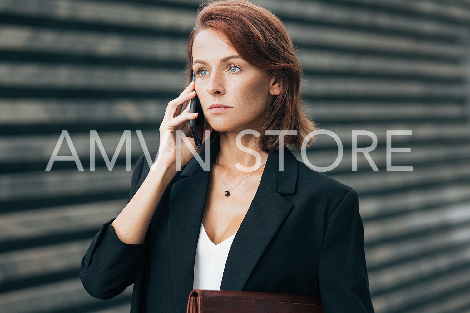 Confident and serious businesswoman with ginger hair talking on mobile phone