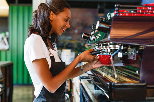 Side view of a smiling female barista making coffee at a cafe