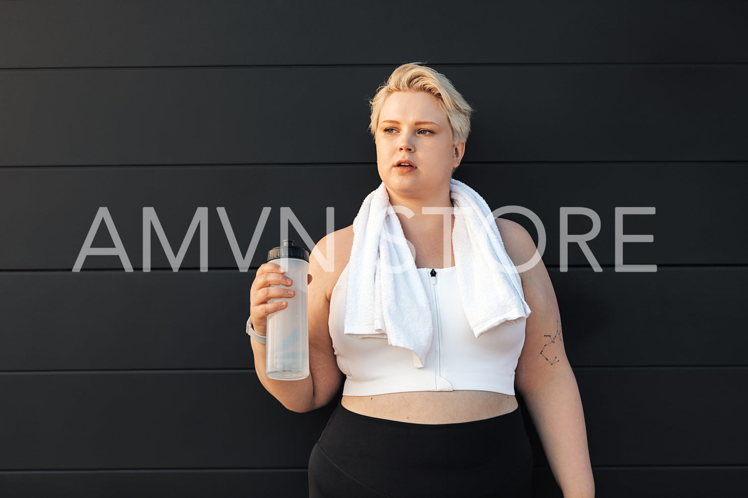 Portrait of a tired curvy woman standing at wall with a towel around a neck