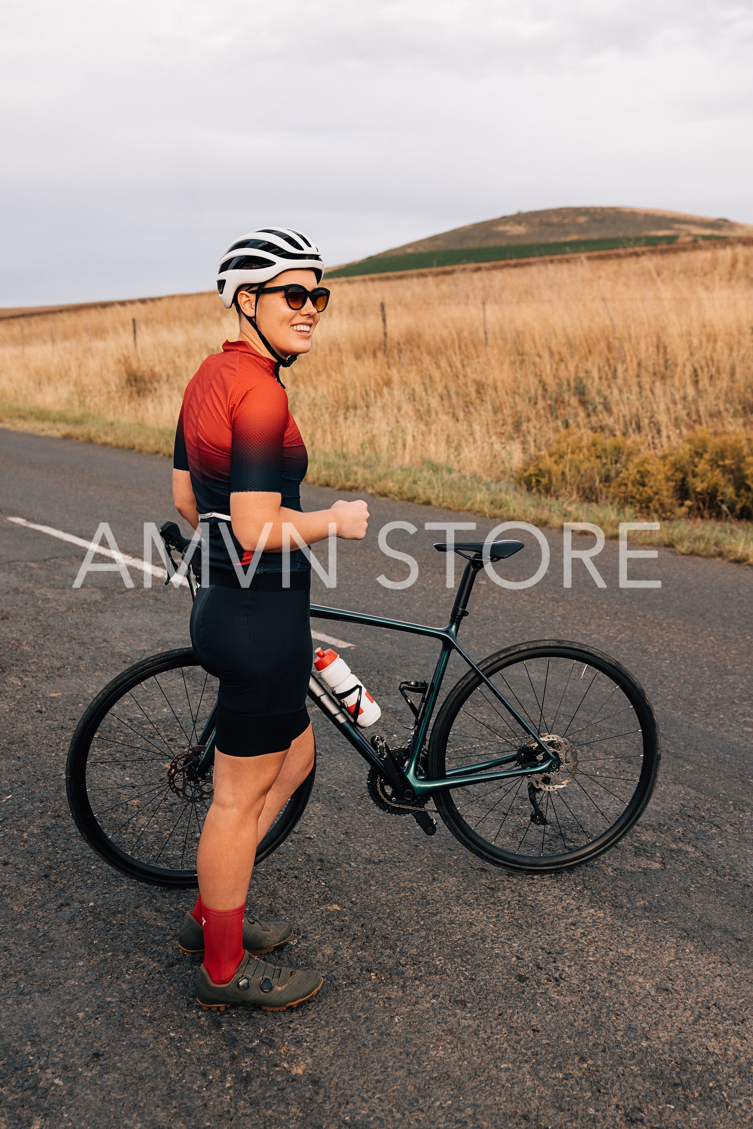 Full length of female cyclist with a bicycle standing on country road and looking away