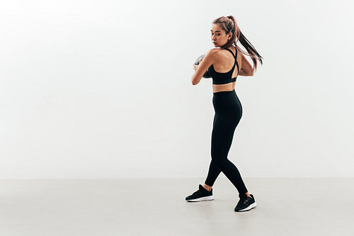 Young muscular woman doing exercises with a medicine ball against a white wall