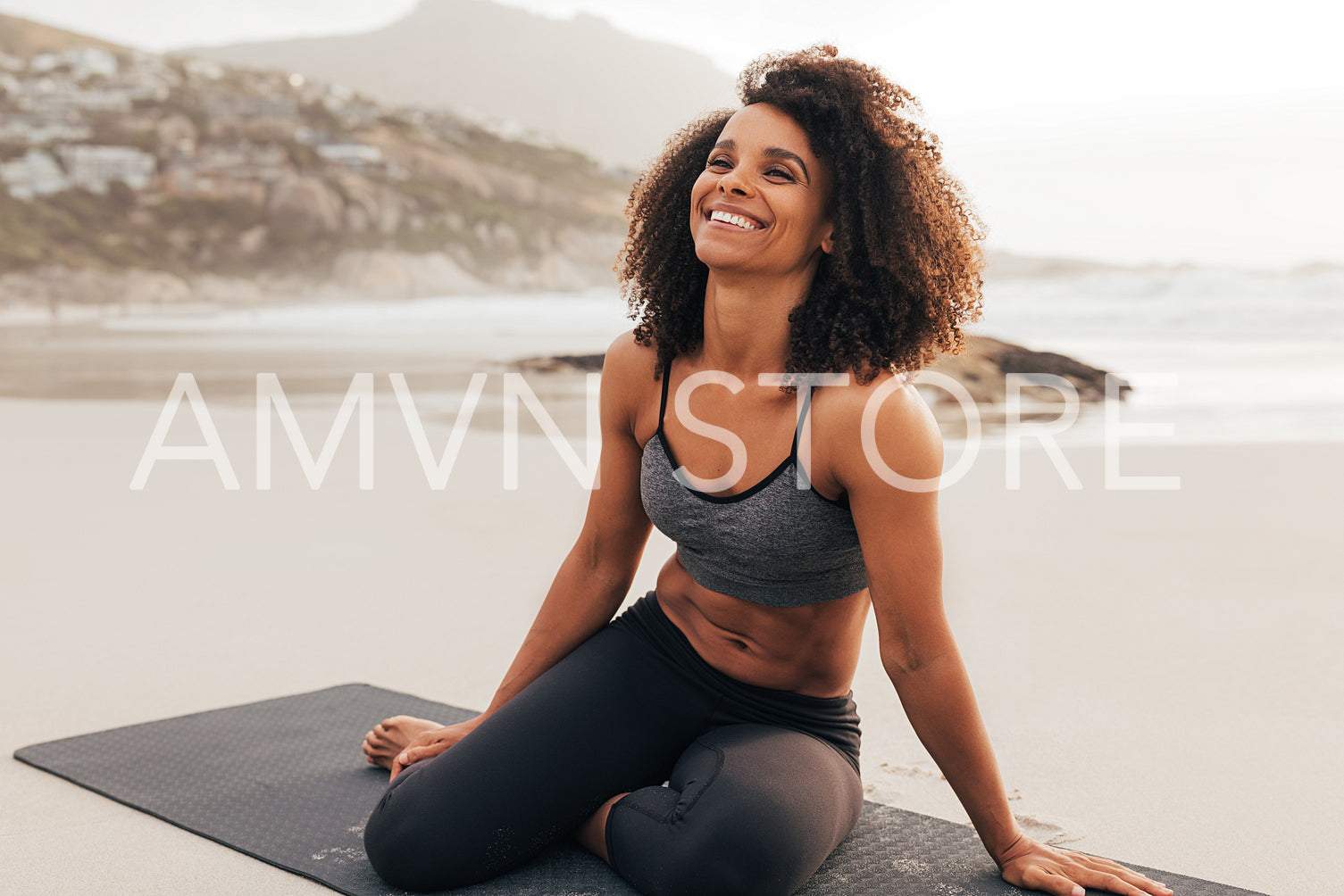 Happy woman in sportswear sitting on beach. Laughing female relaxing after yoga exercises at sunset.