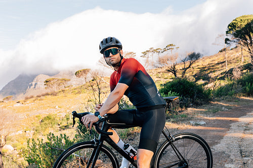 Portrait of a professional cyclist in helmet and glasses standing with bicycle against wild terrain.