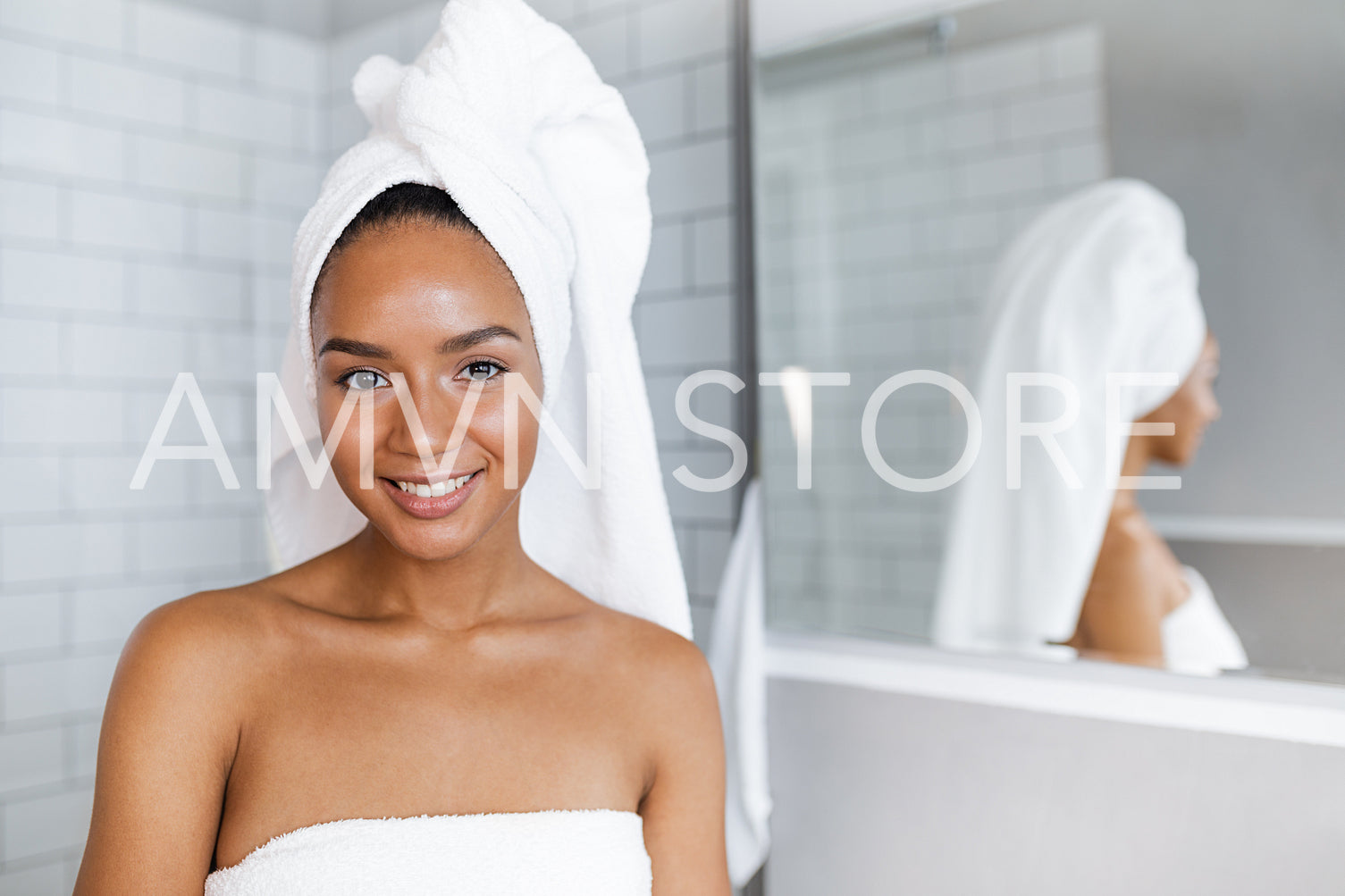 Close up portrait of a beautiful woman in towels wrapped around head and body, standing in bathroom	