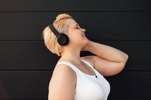 Plus size woman listening to music near a black wall. Young curvy female taking a break during exercises.