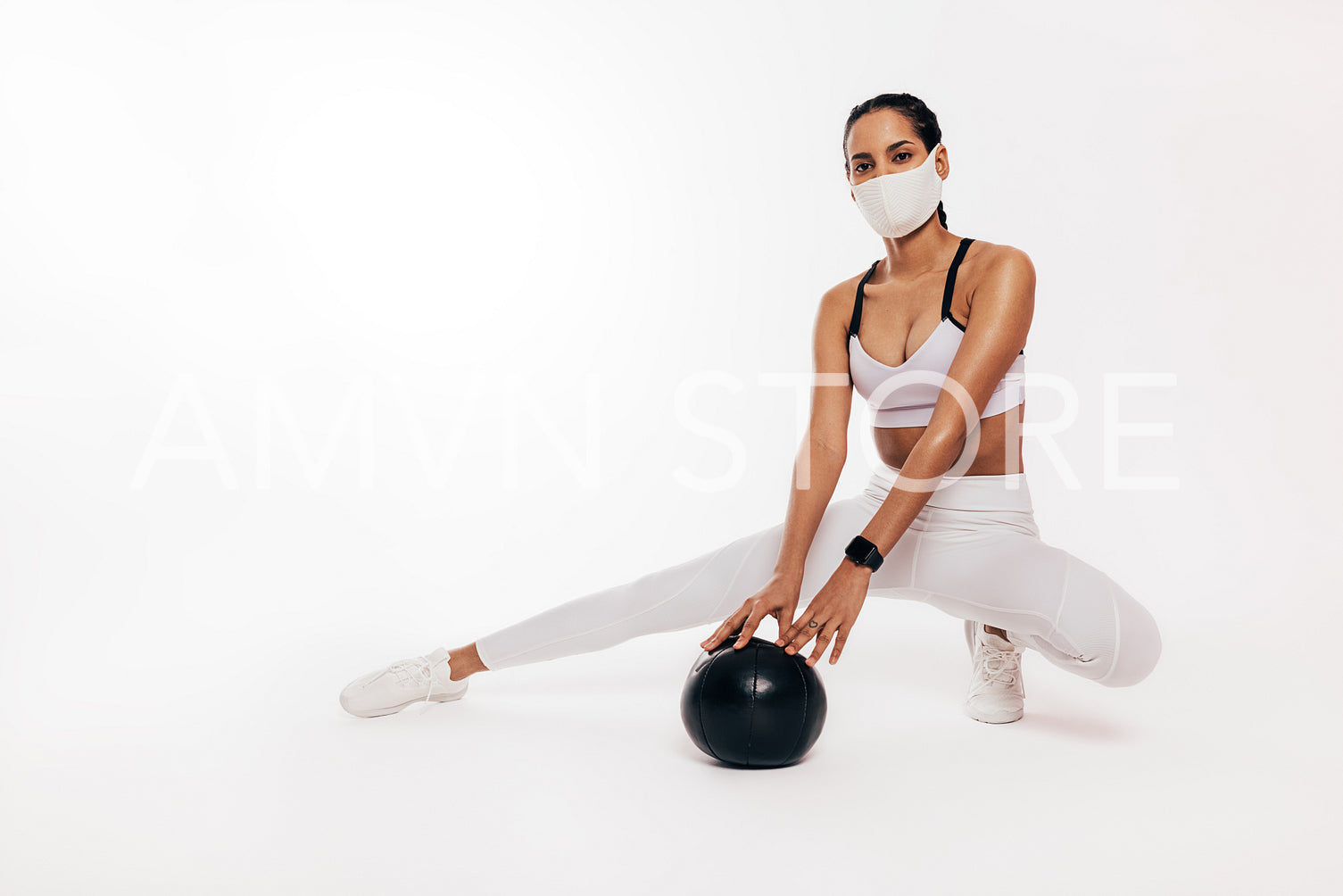 Mixed race woman with face mask sitting in a studio with a medicine ball