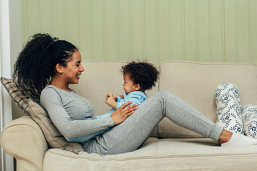 Side view of mother lying on couch and playing with her son