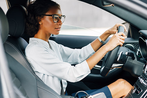 Woman driving a car. Side view of a female driver wearing glasses and looking away.