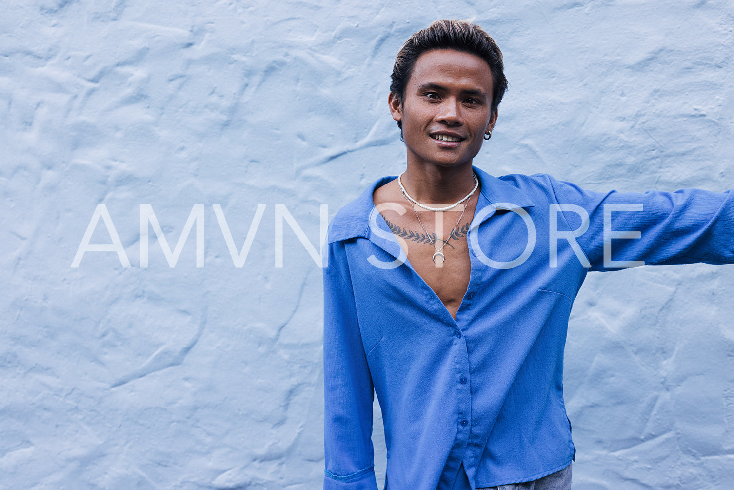 Smiling stylish guy in a blue shirt posing against a blue wall