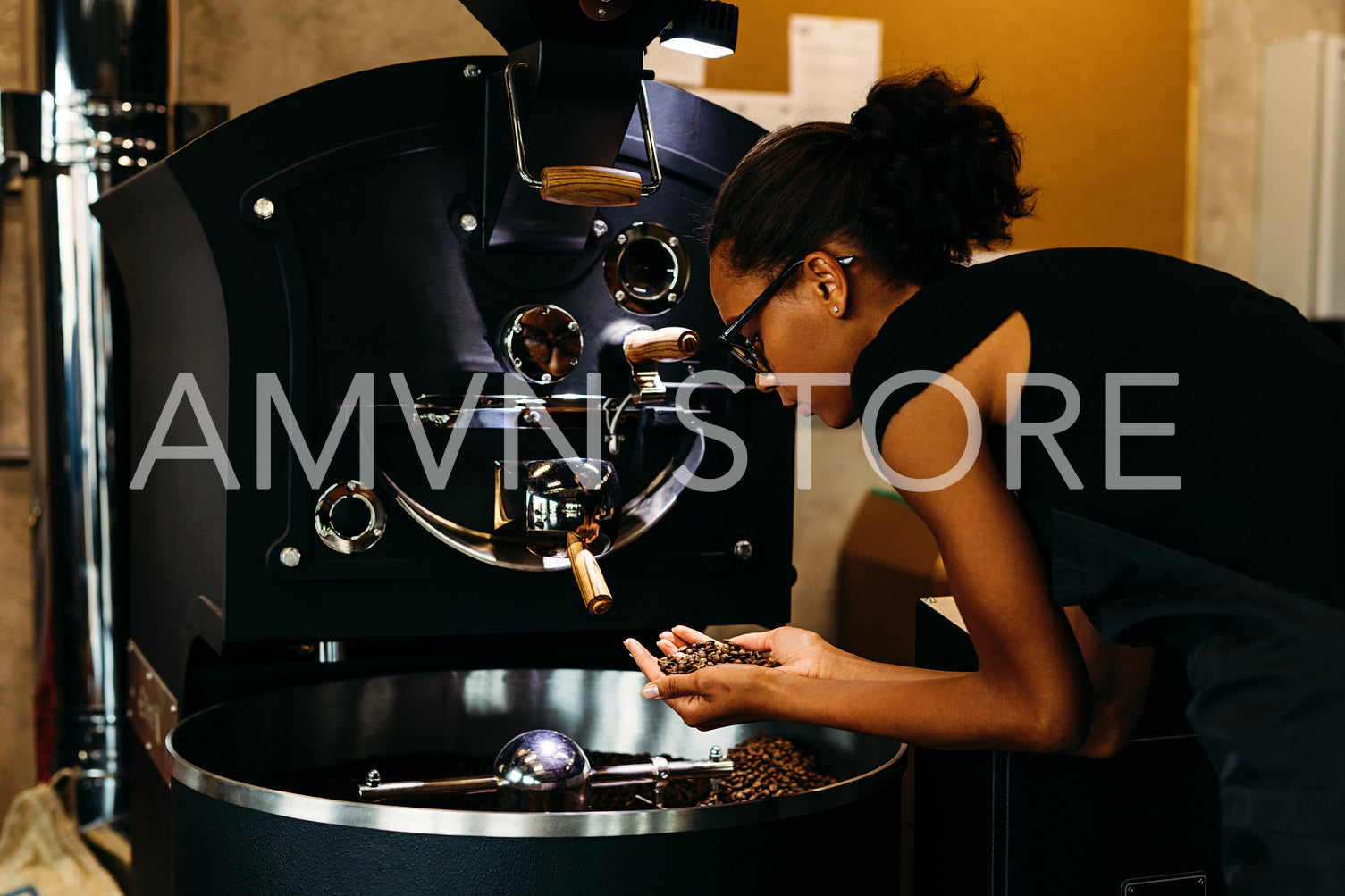 Young barista checking coffee beans in roasting machine, standing in coffee shop	