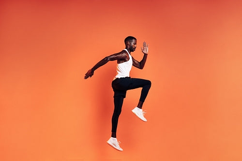 Fit man jumping in studio. Male runnner warming up before workout against orange background