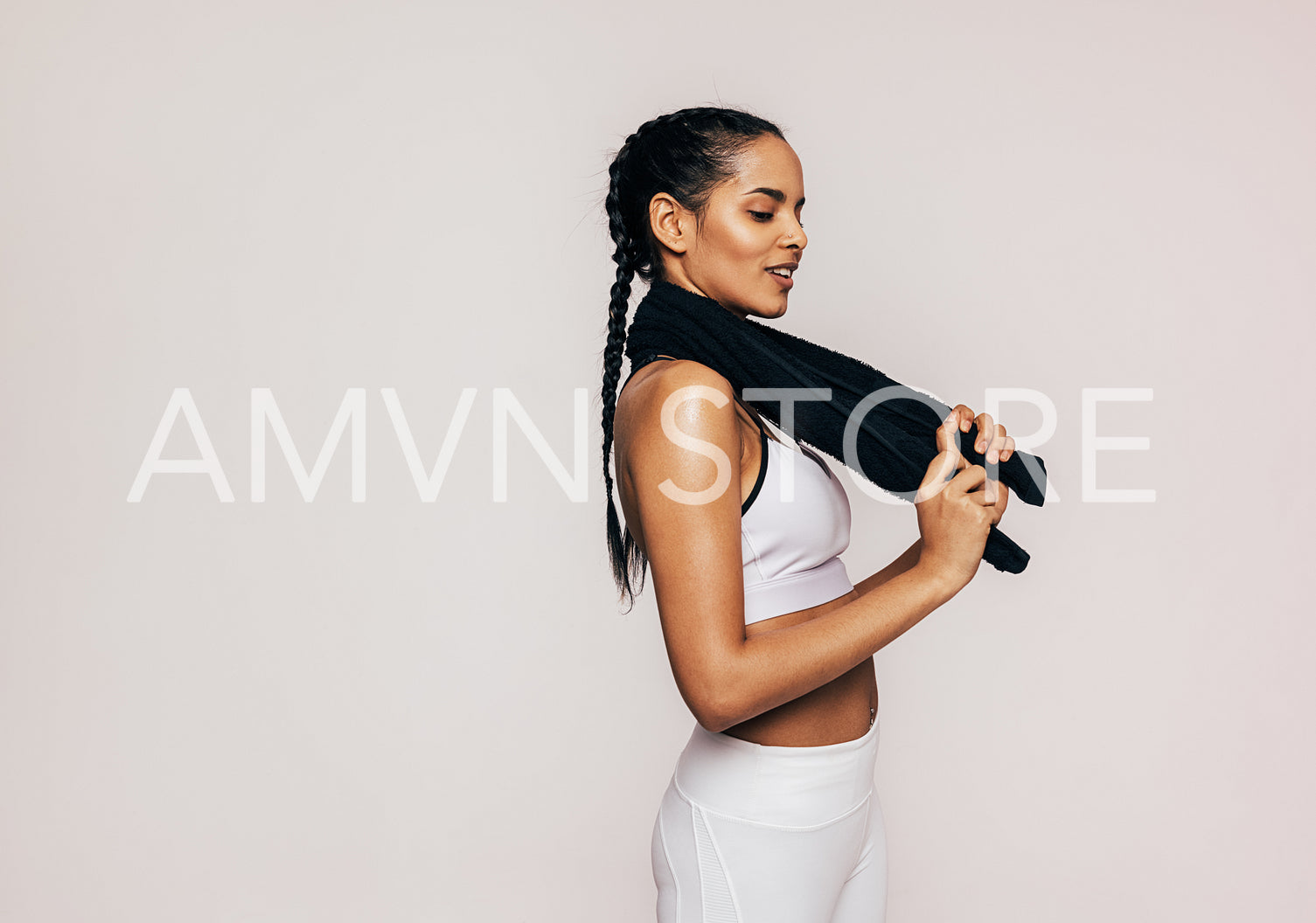 Smiling sportswoman with braids holding a black towel over white background in studio	