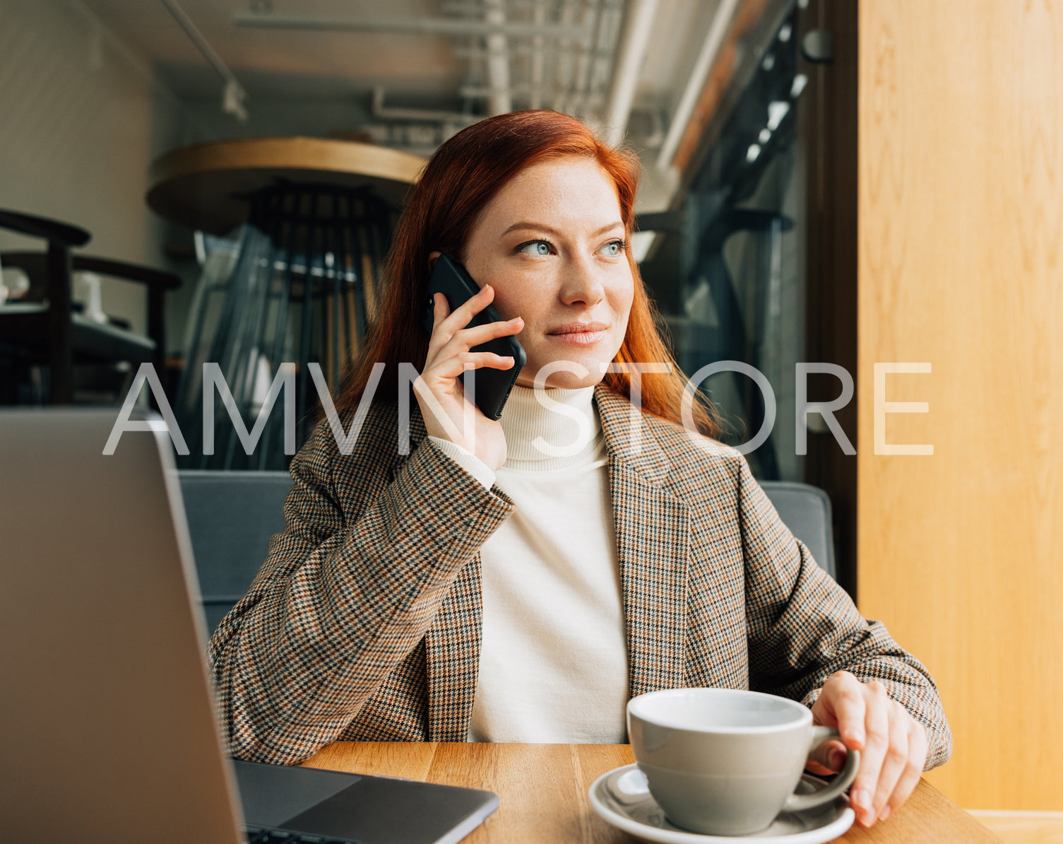 Beautiful businesswoman with ginger hair talking on smartphone and looking at window at a cafe