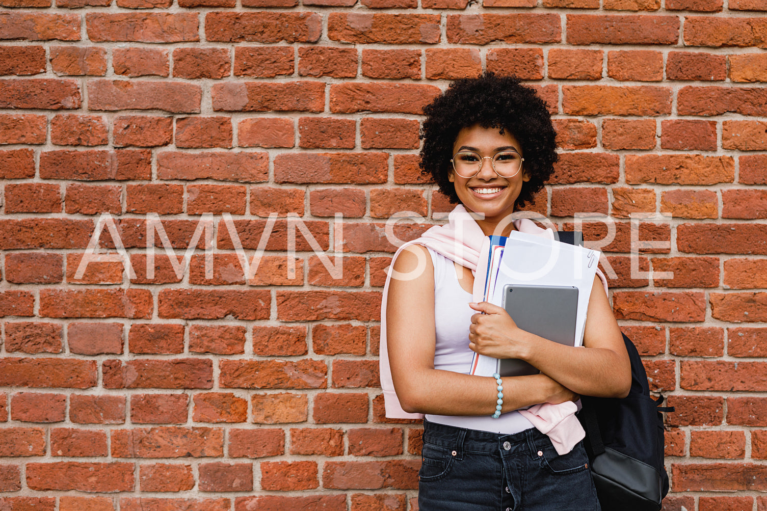 Smiling school girl with books standing at building wall	