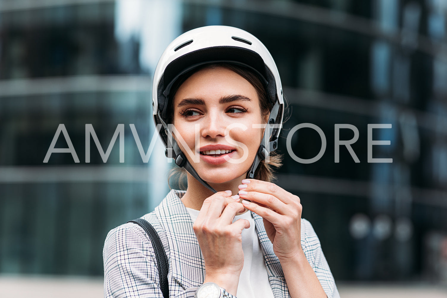 Smiling businesswoman strapping on a cycling helmet while standing in the city. Young female putting a white helmet on her head.