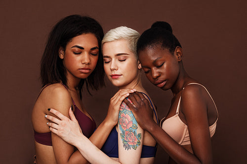 Three diverse women in bras standing with closed eyes over brown