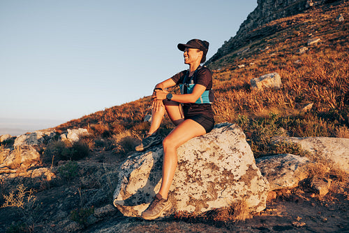 Smiling woman sitting on stone on a mountain relaxing during hike at sunset