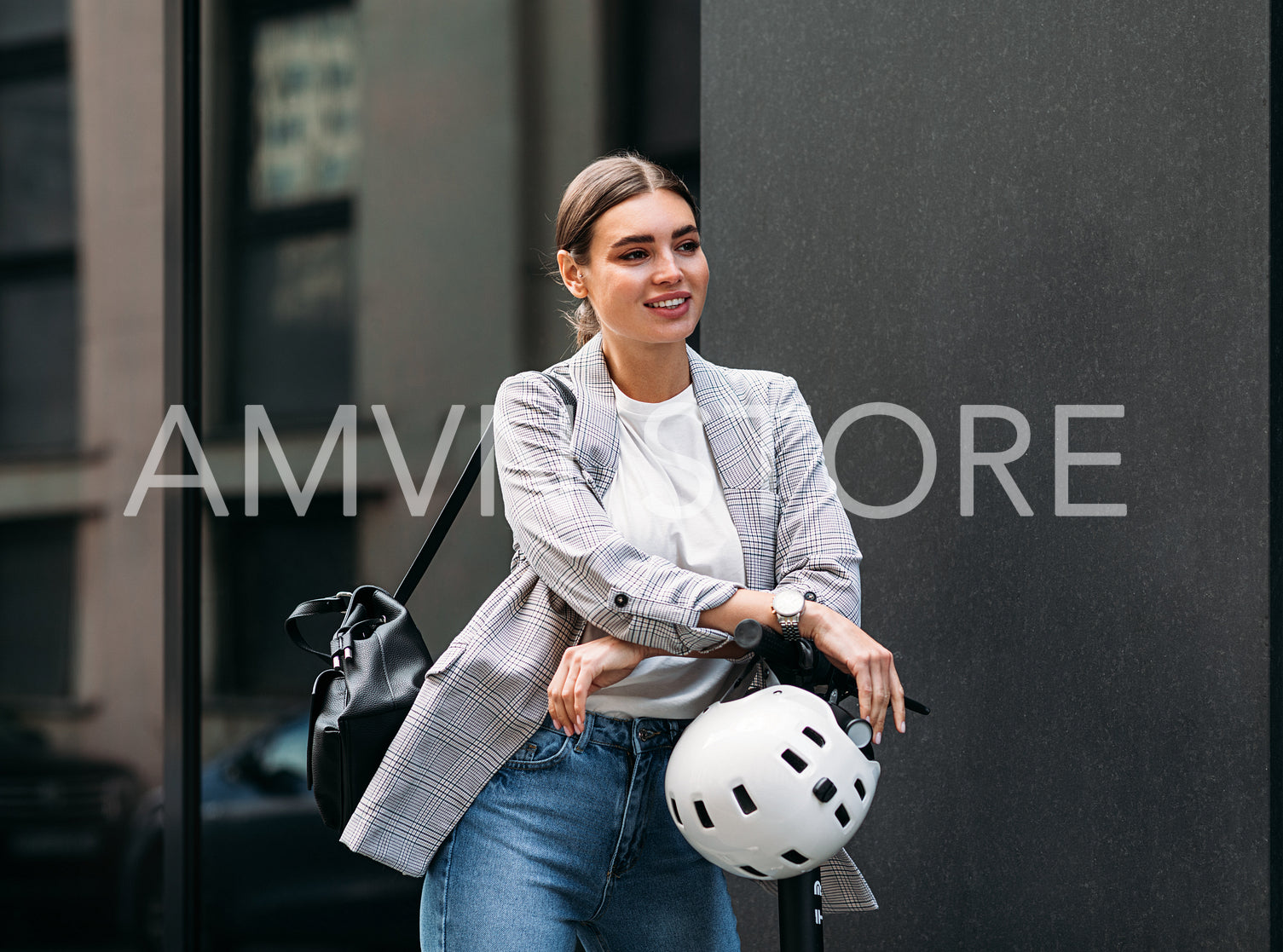 Businesswoman with backpack leaning on the handlebar of electric scooter looking away while standing at a black wall