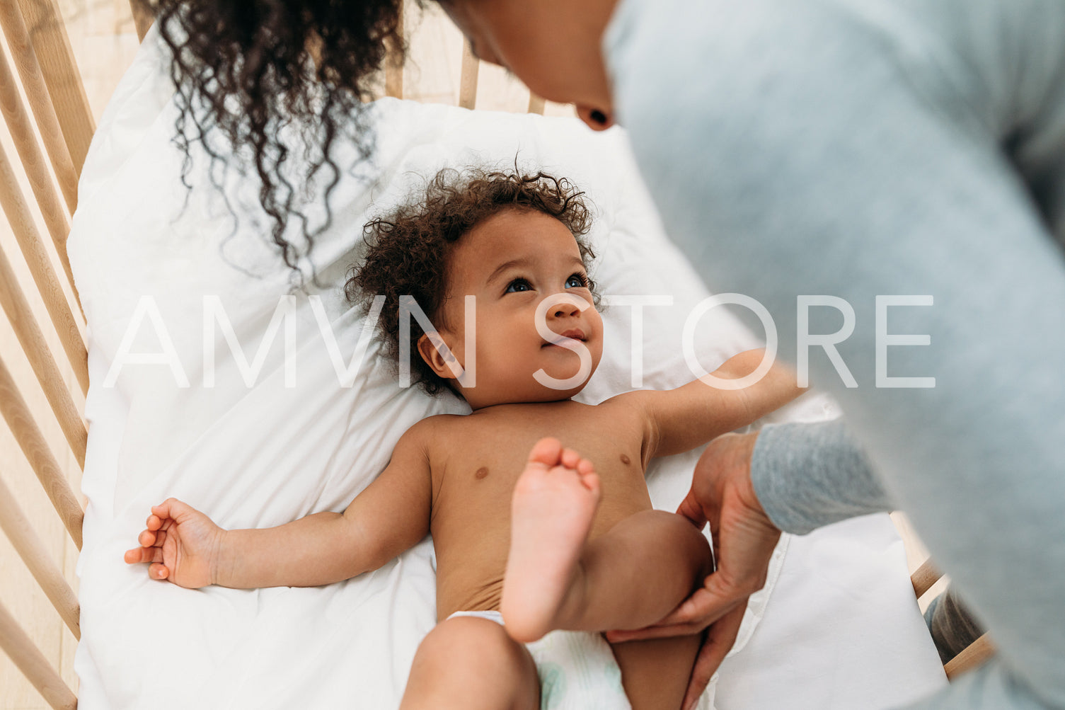 Woman touching leg of a newborn baby boy lying in a crib	