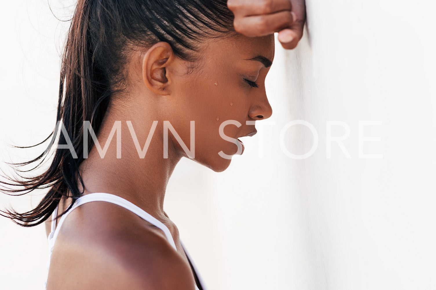 Tired and sweating woman relaxing at white wall. Close-up of a female with closed eyes leaning on her hand taking a break during a workout.