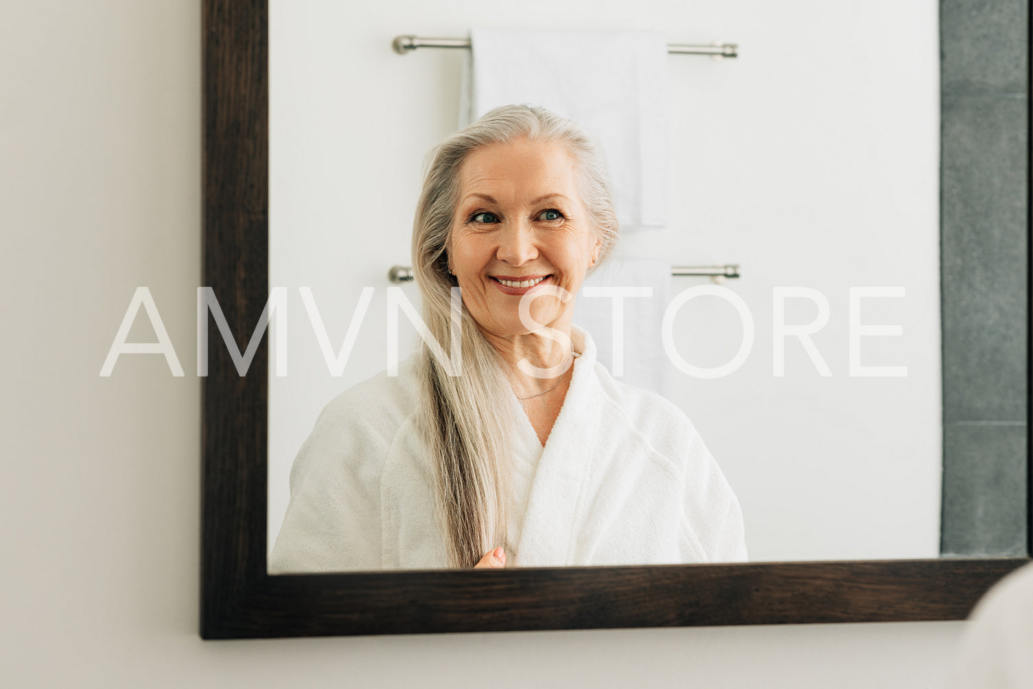 Smiling woman with long grey hair looking at a mirror in bathroom