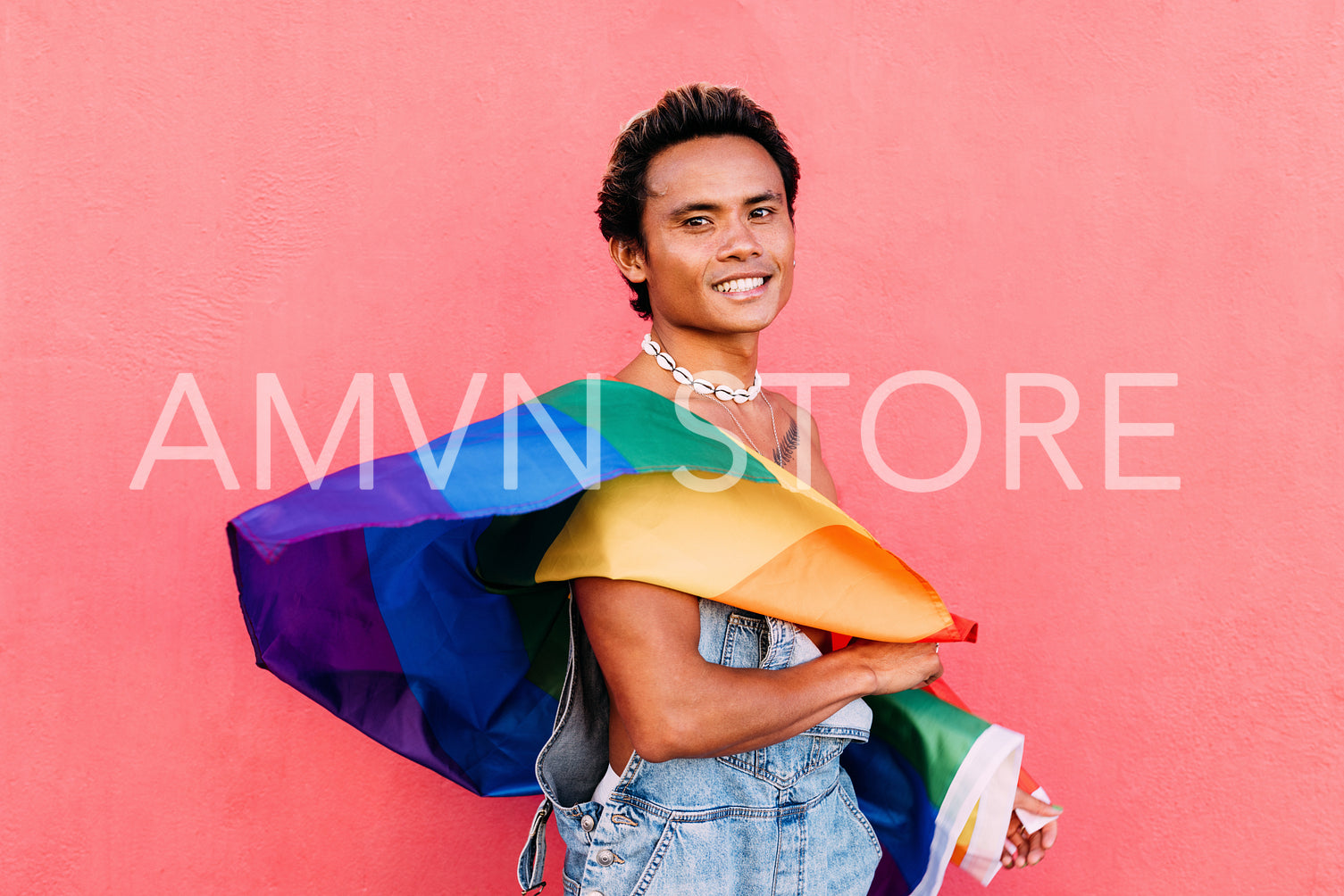 Portrait of a young smiling guy posing with LGBT flag against pink wall outdoors