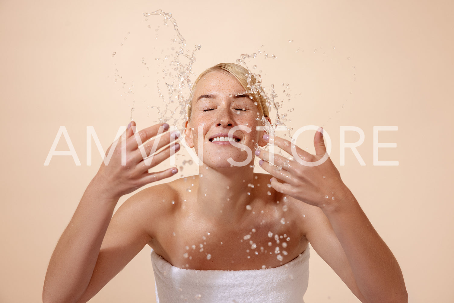 Cheerful blonde woman in white towel splashing water on her face