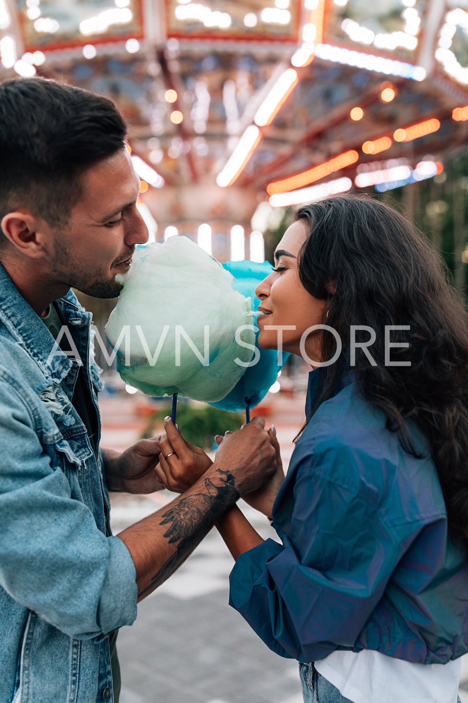 Young couple biting cotton candy during a date in an amusement park