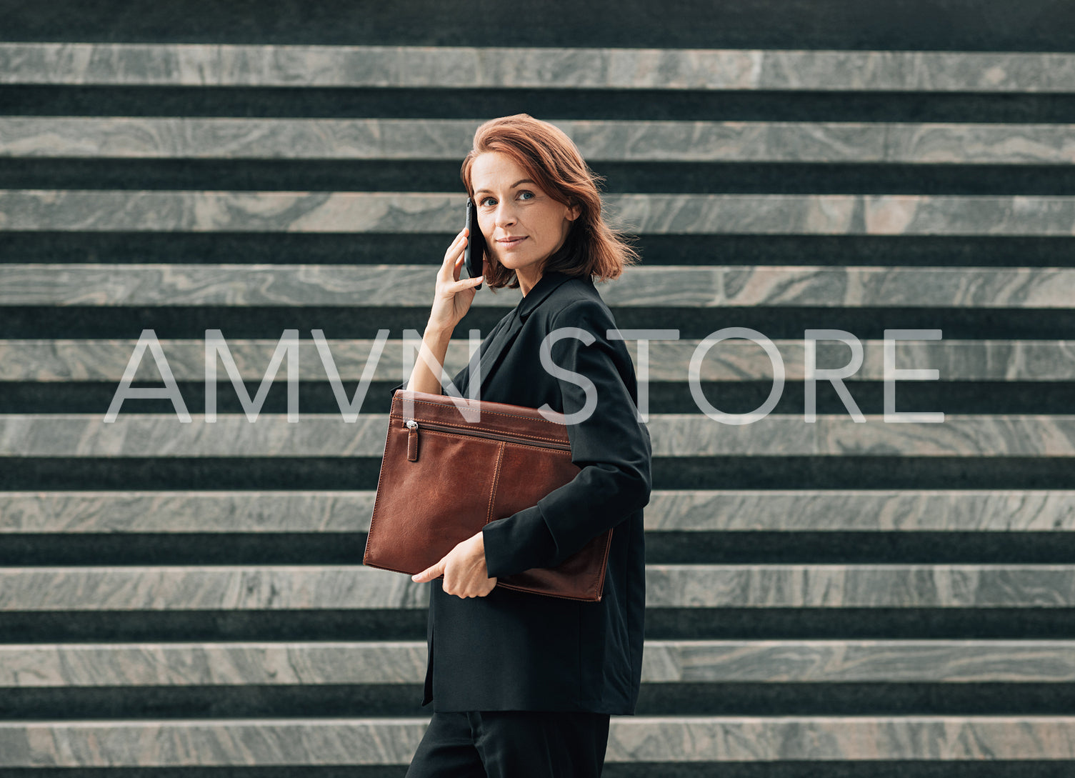 Side view of a confident middle-aged female with a leather folder. Businesswoman with ginger hair making a phone call while standing outdoors.