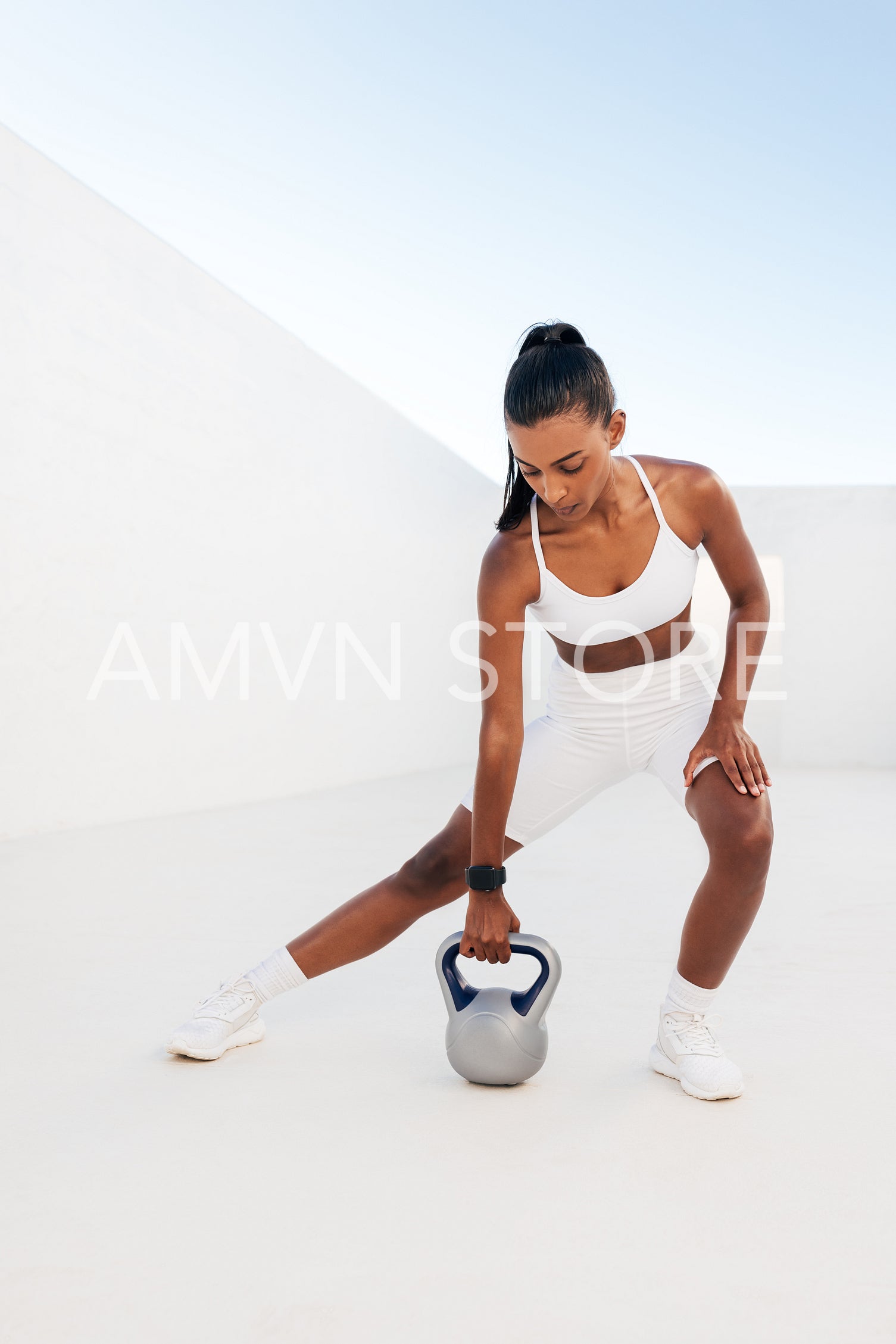 Young fit female doing a workout with a kettlebell. Woman exercising in a white outdoor studio with weights.