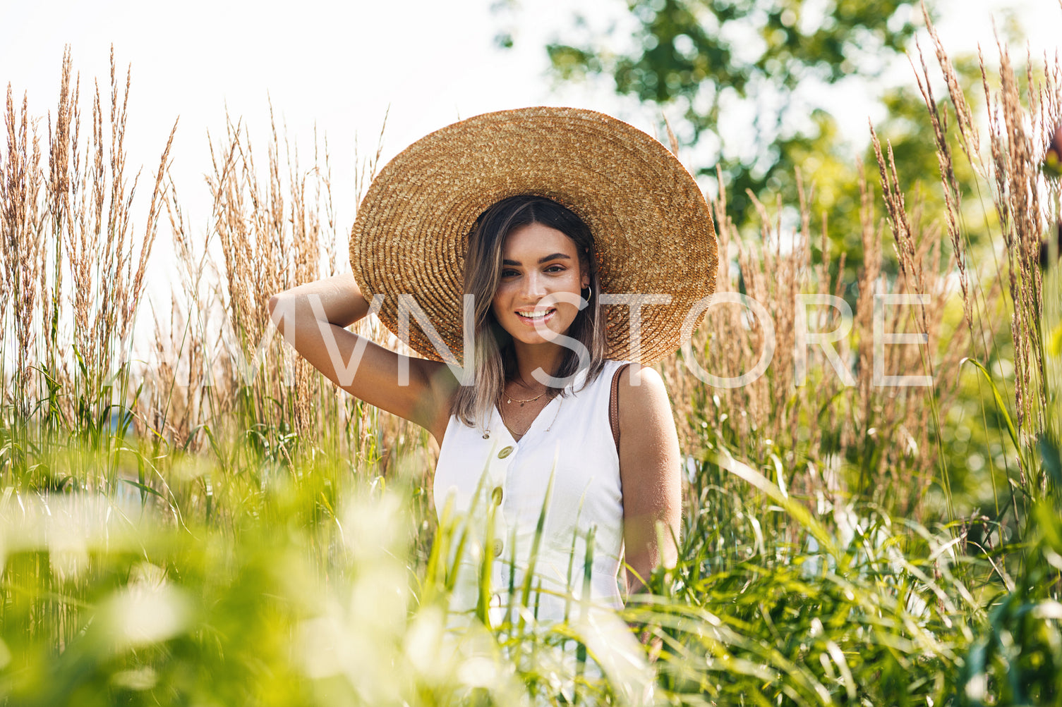 Young cheerful woman wearing big straw hat and looking at camera	