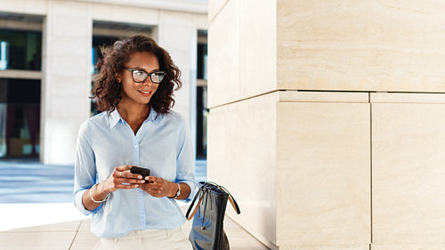 Smiling woman with smartphone in her hands. Entrepreneur standing outdoors and looking away.