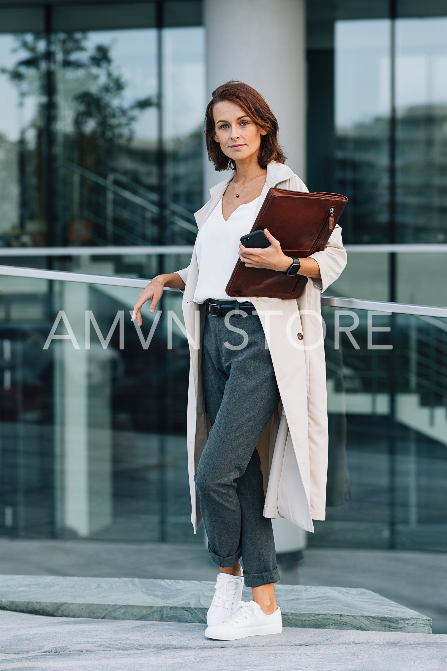 Confident middle-aged female holding a leather folder looking at camera standing at an office building