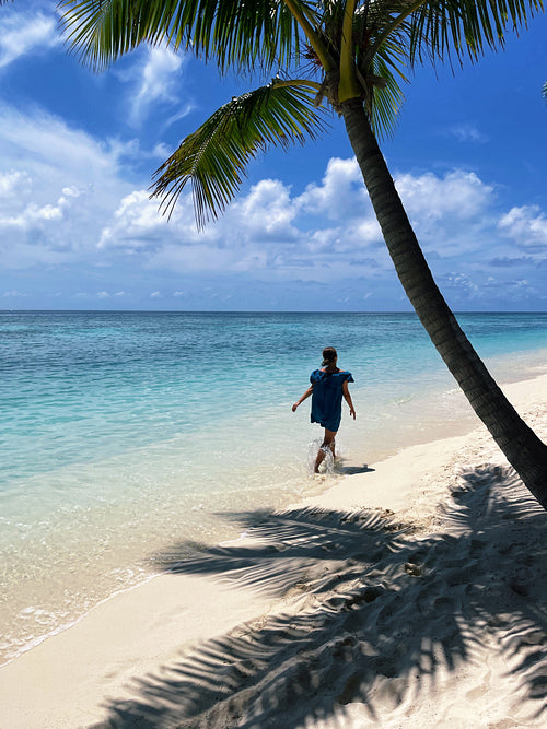 Back view of young woman walking on a tropical beach