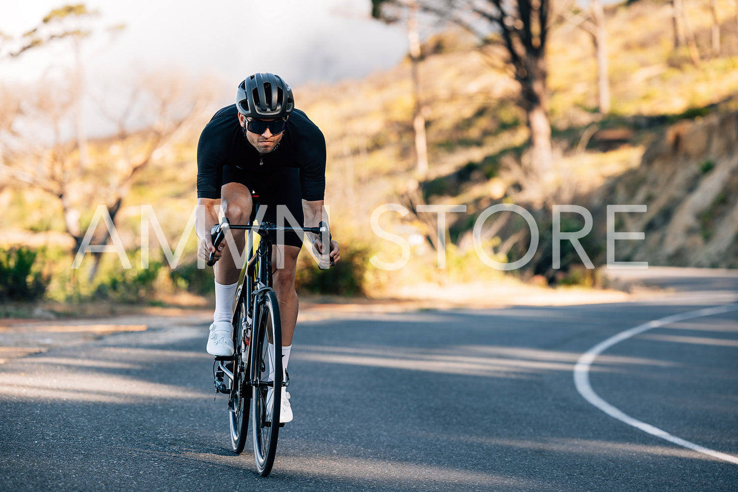 Professional cyclist in black sports attire going down a hill. Cyclist in a helmet and glasses riding on a bicycle outdoors.